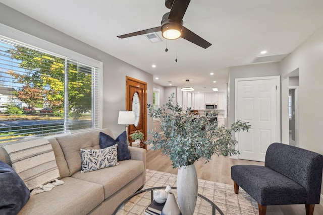 living room featuring light wood finished floors, a ceiling fan, visible vents, and recessed lighting