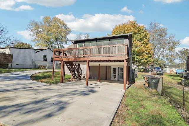 rear view of property featuring fence, concrete driveway, french doors, stairway, and a wooden deck