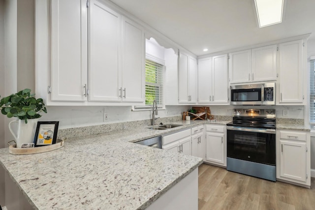 kitchen featuring light wood finished floors, a peninsula, stainless steel appliances, white cabinetry, and a sink