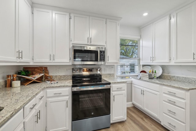 kitchen with light wood finished floors, white cabinetry, appliances with stainless steel finishes, and light stone counters