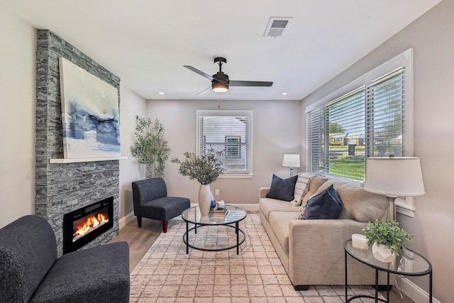 living area featuring light wood-style flooring, visible vents, a stone fireplace, and baseboards