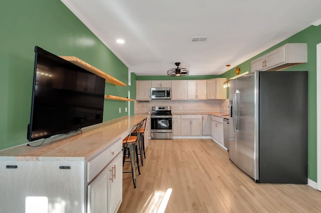 kitchen with tasteful backsplash, light countertops, appliances with stainless steel finishes, and light wood-style floors