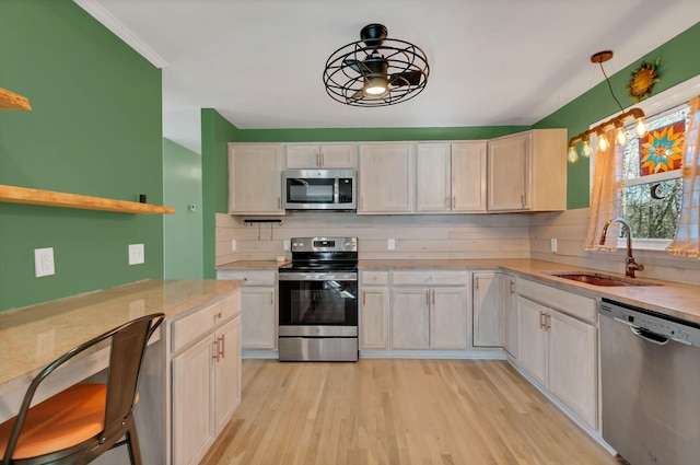 kitchen featuring light wood-style flooring, a sink, light countertops, appliances with stainless steel finishes, and decorative backsplash