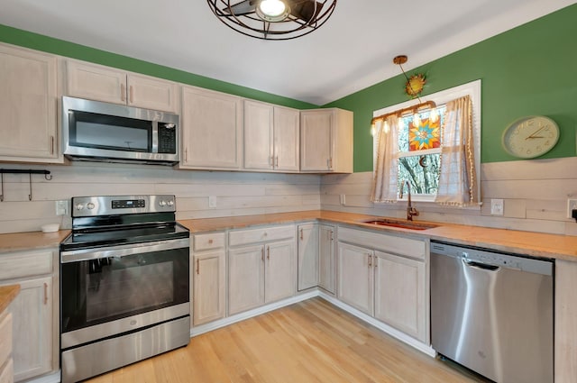 kitchen with stainless steel appliances, a sink, light countertops, light wood-type flooring, and tasteful backsplash