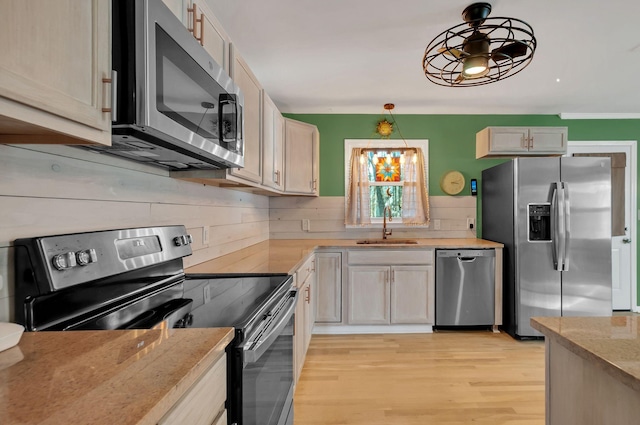 kitchen with a sink, light wood-style floors, appliances with stainless steel finishes, light stone countertops, and pendant lighting