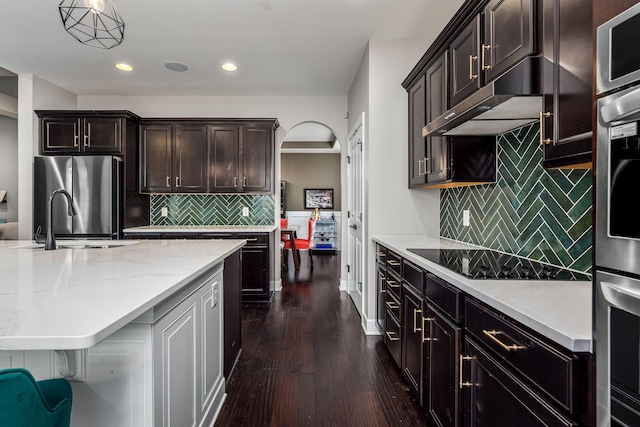 kitchen featuring arched walkways, dark wood-style flooring, freestanding refrigerator, black electric stovetop, and under cabinet range hood