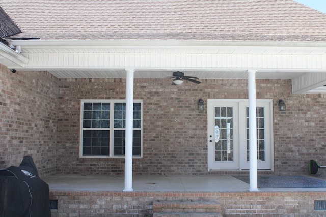 entrance to property featuring ceiling fan, brick siding, a patio, and roof with shingles