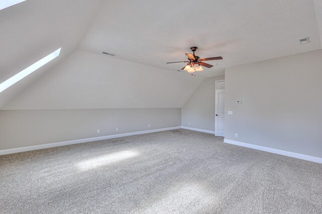 additional living space featuring visible vents, carpet floors, lofted ceiling with skylight, and a ceiling fan