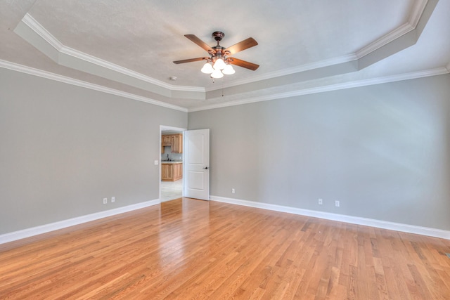 empty room with light wood finished floors, crown molding, baseboards, ceiling fan, and a raised ceiling