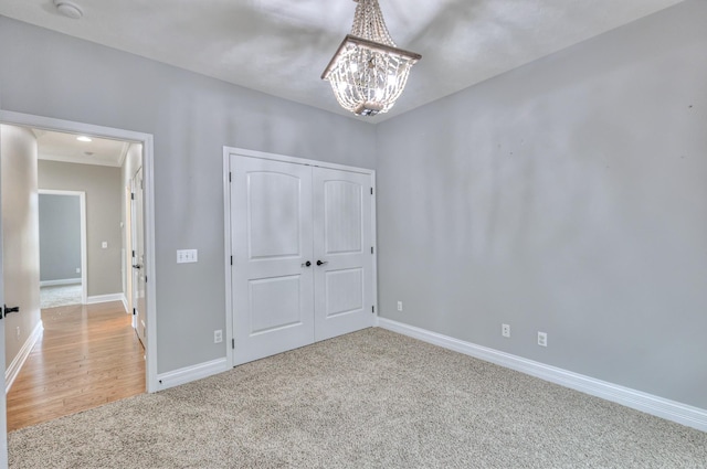 unfurnished bedroom featuring a closet, a notable chandelier, baseboards, and carpet floors