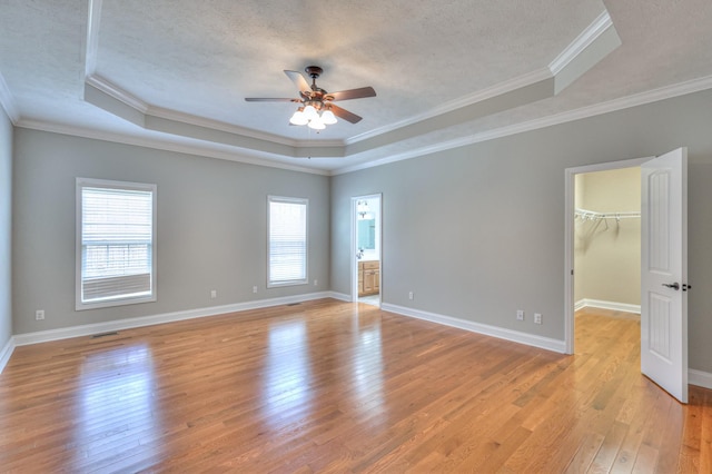 spare room with a textured ceiling, a ceiling fan, light wood-style floors, and a tray ceiling