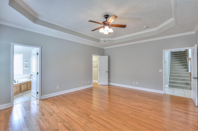 unfurnished bedroom featuring a tray ceiling, baseboards, a spacious closet, and light wood finished floors