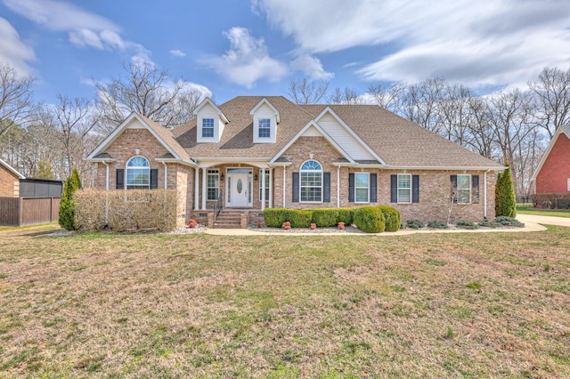 view of front facade with a front yard, fence, brick siding, and roof with shingles