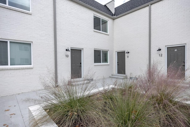 entrance to property with a shingled roof and brick siding