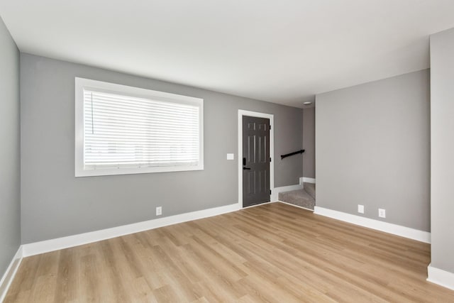 empty room featuring baseboards, stairway, and light wood finished floors