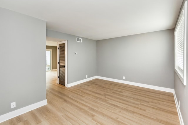 spare room featuring visible vents, light wood-type flooring, a wealth of natural light, and baseboards