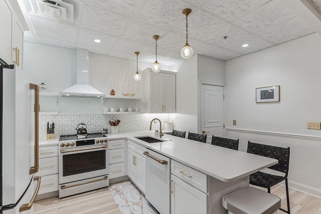 kitchen featuring white appliances, a breakfast bar, a sink, decorative backsplash, and wall chimney exhaust hood