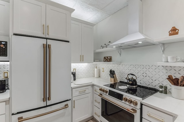 kitchen featuring electric stove, open shelves, light countertops, freestanding refrigerator, and wall chimney range hood