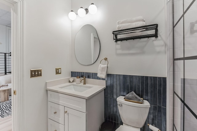 bathroom featuring a wainscoted wall, a tile shower, vanity, and toilet