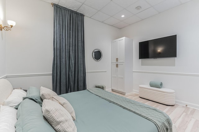 bedroom featuring light wood-style floors, a paneled ceiling, and baseboards