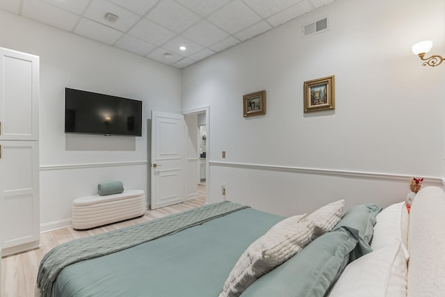 bedroom with light wood finished floors, a drop ceiling, visible vents, and baseboards