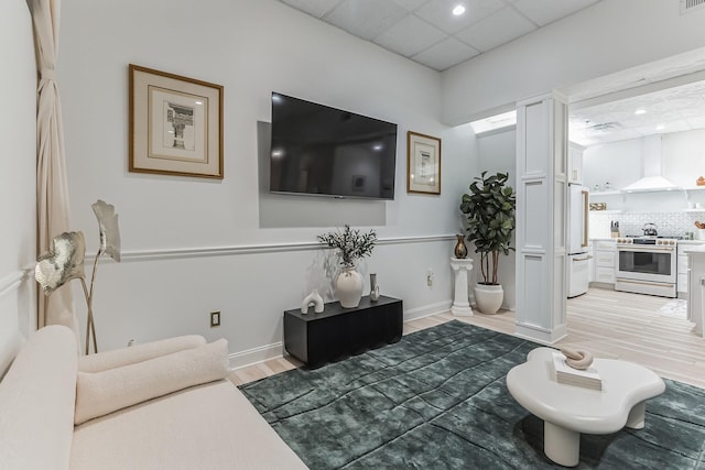 living area with a paneled ceiling, light wood-style floors, and baseboards