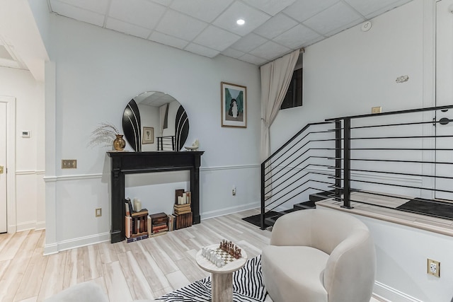 sitting room featuring stairs, a paneled ceiling, baseboards, and wood finished floors