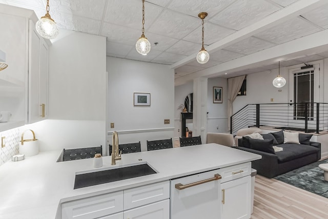 kitchen featuring a peninsula, a sink, decorative light fixtures, and white cabinets