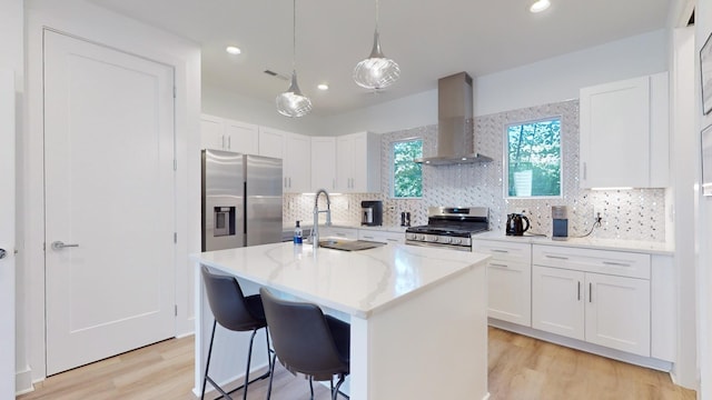 kitchen with light wood finished floors, decorative backsplash, appliances with stainless steel finishes, white cabinets, and wall chimney range hood