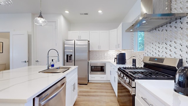 kitchen with backsplash, appliances with stainless steel finishes, white cabinetry, a sink, and wall chimney exhaust hood