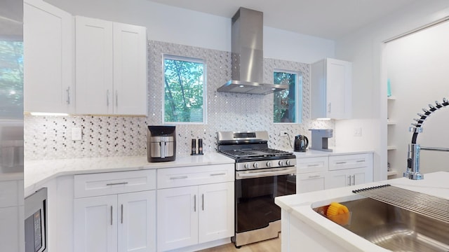 kitchen featuring white cabinetry, light countertops, wall chimney range hood, decorative backsplash, and stainless steel range with gas stovetop