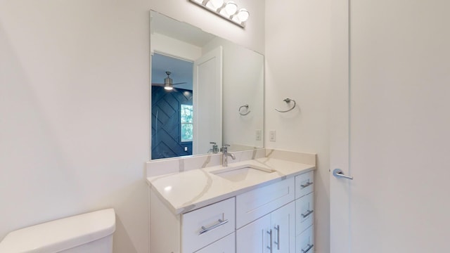 half bathroom with toilet, ceiling fan, and vanity