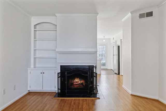 unfurnished living room with a warm lit fireplace, visible vents, baseboards, built in features, and light wood-style flooring