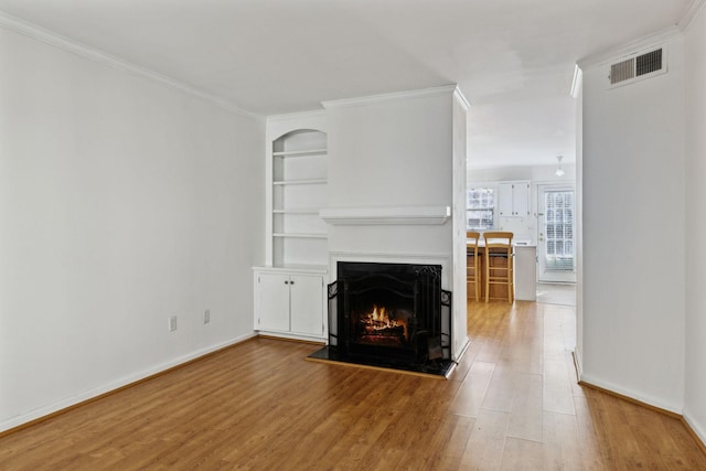 unfurnished living room with built in shelves, wood finished floors, visible vents, a lit fireplace, and ornamental molding