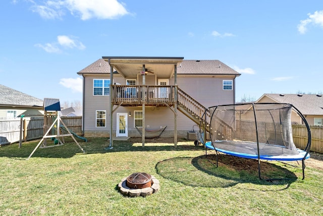 rear view of property with a deck, a fenced backyard, a fire pit, a yard, and a trampoline