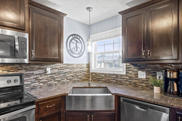 kitchen with a textured ceiling, stainless steel appliances, a sink, dark brown cabinets, and backsplash