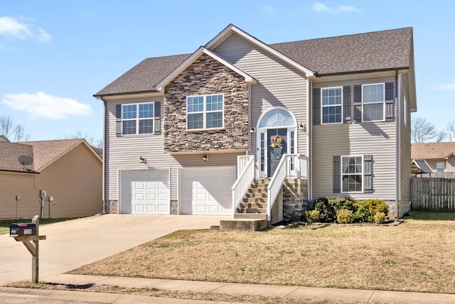 bi-level home with a garage, concrete driveway, stone siding, roof with shingles, and a front yard