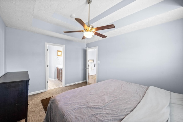 carpeted bedroom featuring a tray ceiling, ceiling fan, a textured ceiling, ensuite bath, and baseboards