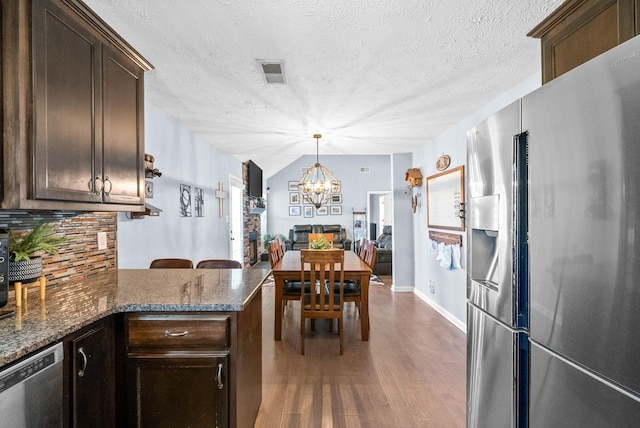 kitchen featuring stainless steel appliances, wood finished floors, visible vents, dark brown cabinets, and decorative backsplash