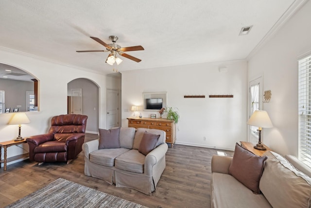 living area featuring baseboards, arched walkways, wood finished floors, and ornamental molding