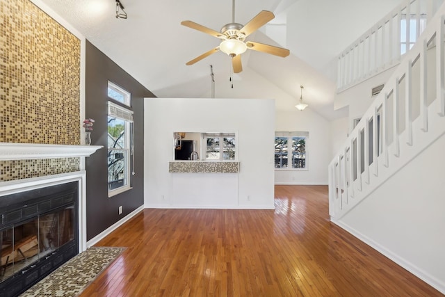 unfurnished living room featuring baseboards, a tiled fireplace, hardwood / wood-style floors, and stairs