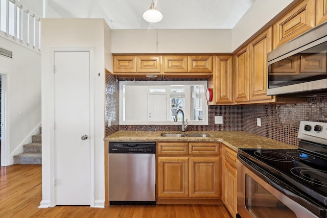 kitchen featuring light wood finished floors, appliances with stainless steel finishes, a sink, light stone countertops, and backsplash