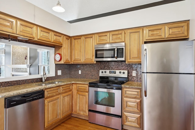 kitchen featuring appliances with stainless steel finishes, light stone countertops, a sink, and tasteful backsplash