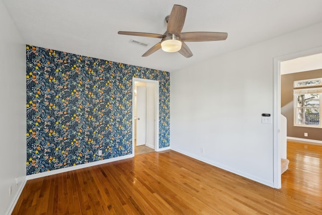 unfurnished room featuring a ceiling fan, visible vents, baseboards, and wood finished floors