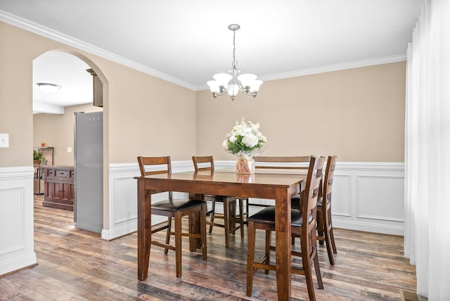 dining area with light wood-type flooring, arched walkways, wainscoting, and crown molding