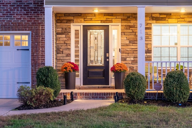 entrance to property with covered porch, brick siding, and an attached garage