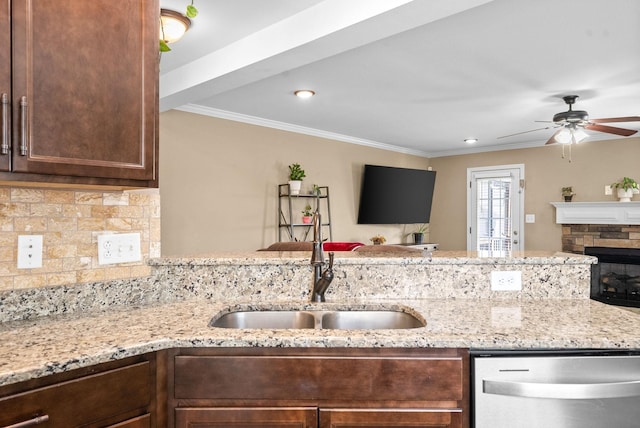 kitchen with a fireplace, a sink, stainless steel dishwasher, backsplash, and light stone countertops