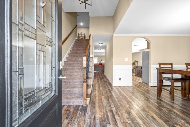 entrance foyer featuring dark wood-style floors, arched walkways, crown molding, and wainscoting