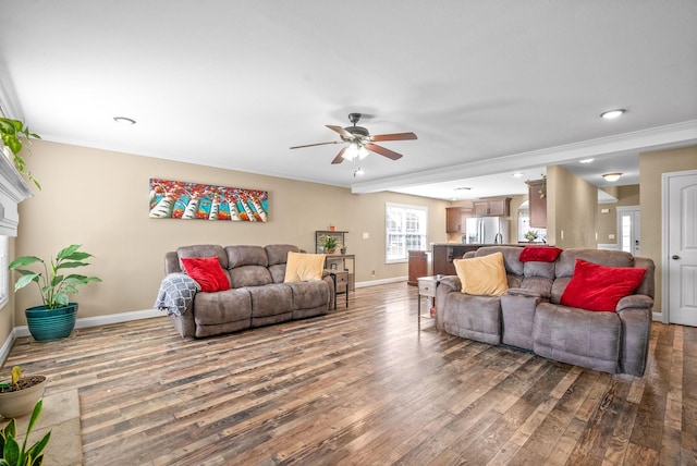 living area with ornamental molding, wood finished floors, a ceiling fan, and baseboards