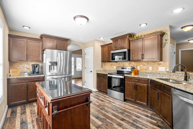 kitchen with tasteful backsplash, arched walkways, dark wood finished floors, stainless steel appliances, and a sink